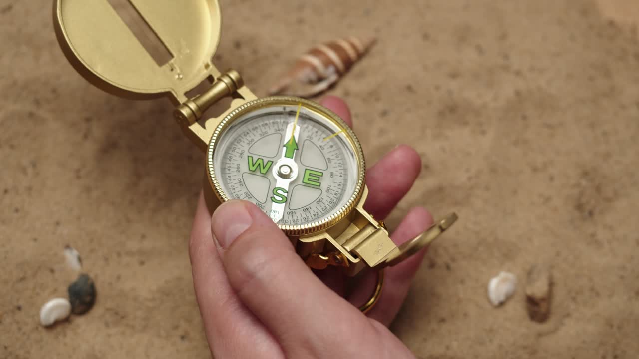 모래 배경에서 금색 나침반을 들고 있는 사람, 손바닥에 달린 금색 나선, 여행과 관광 개념, 항해