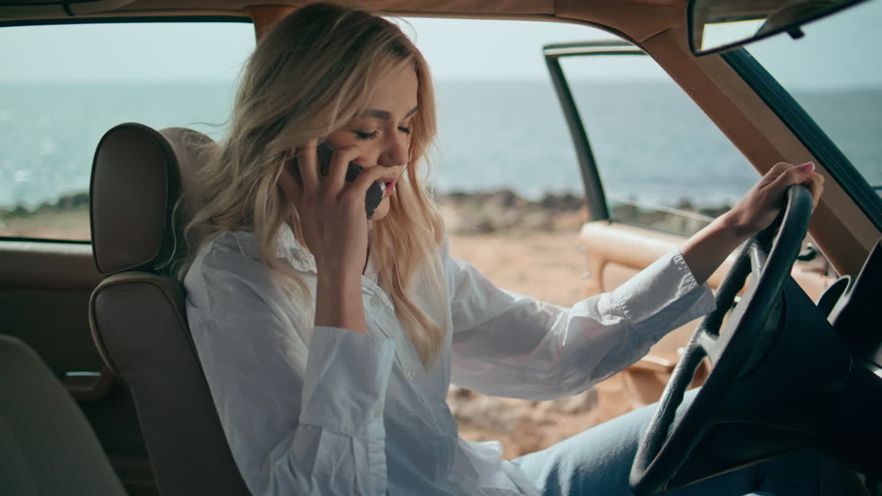 해변에서 빈티지 자동차를 운전하는 동안 전화로 이야기하는 여자