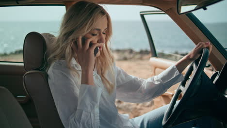 woman talking on phone while driving a vintage car by the beach