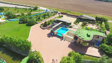 people swimming in the pool and resting around it. aerial footage over the green beautiful resort territory. farmlands at backdrop.