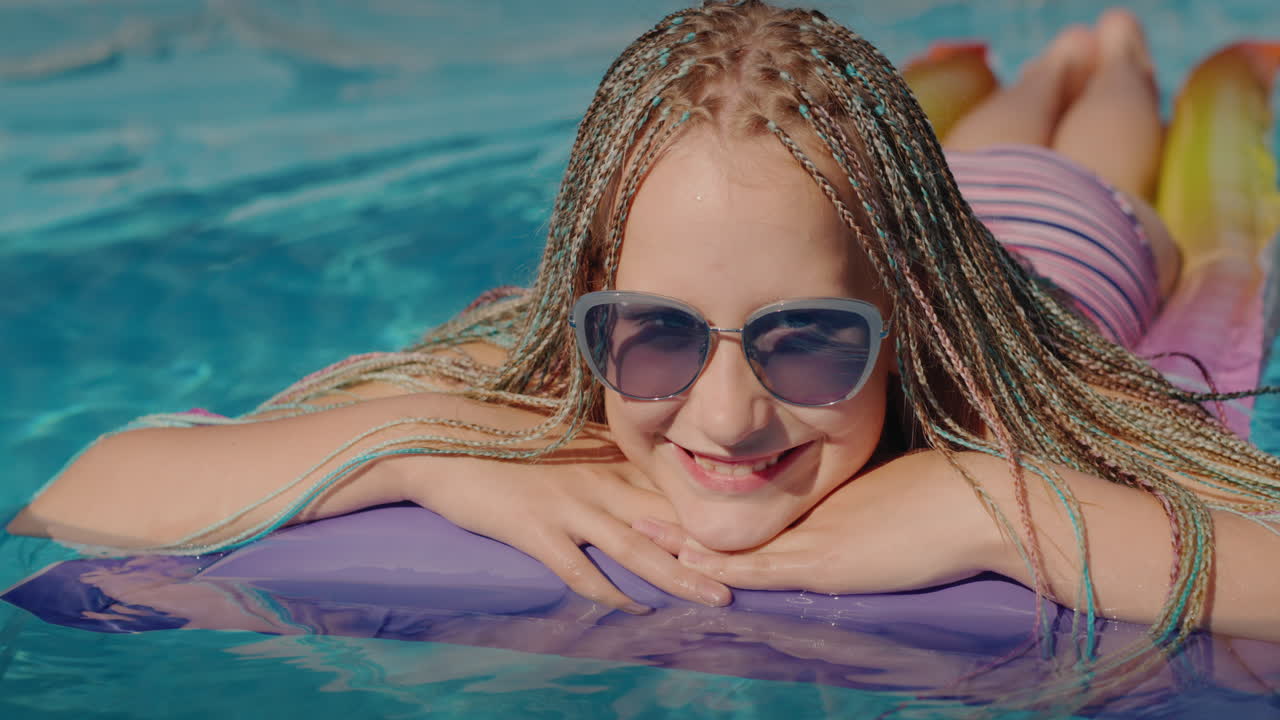 retrato de una chica con coletas afro, nada en un colchón inflable en la piscina, descansando y disfrutando del descanso