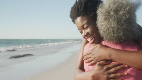 happy senior african american mother and daughter embracing at beach, copy space, in slow motion