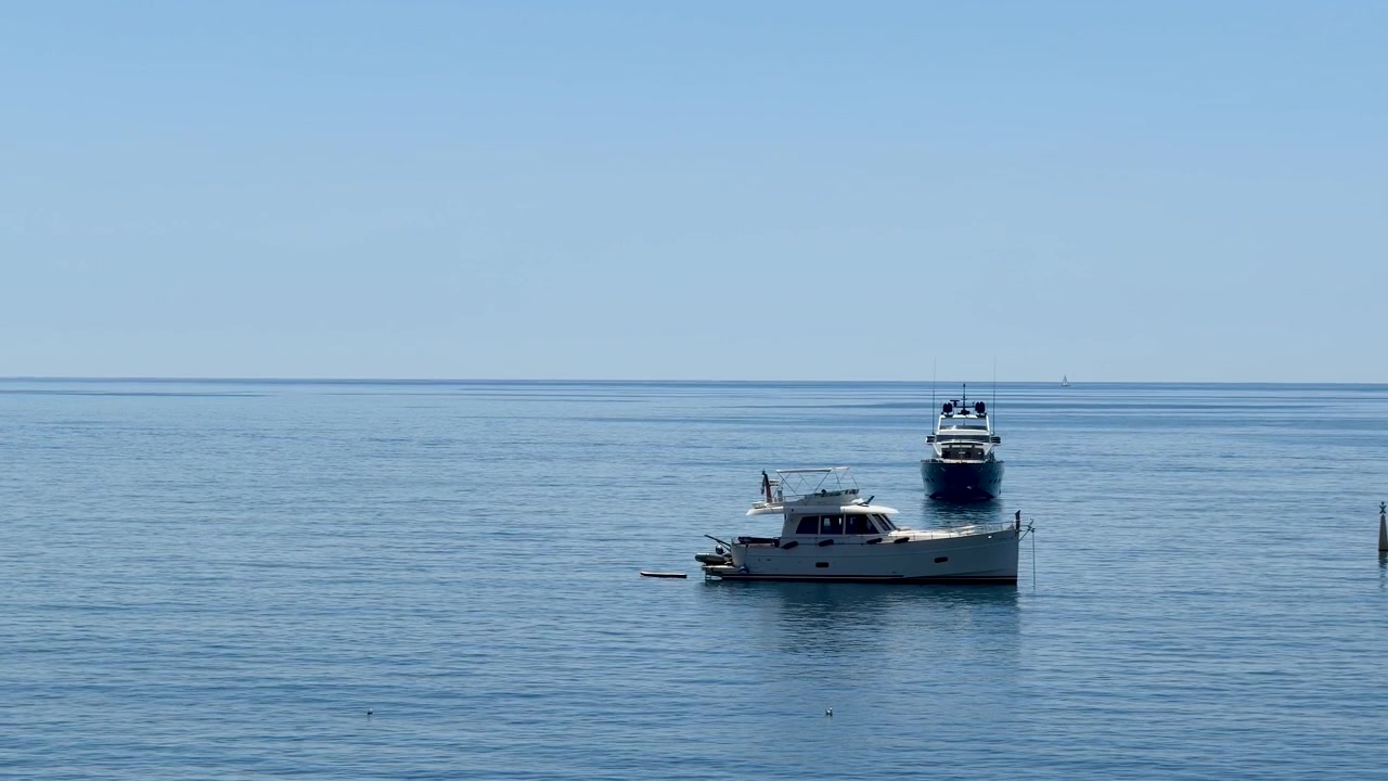 Due yacht di lusso bianchi galleggiano su acque oceaniche blu e calme sotto un cielo sereno.