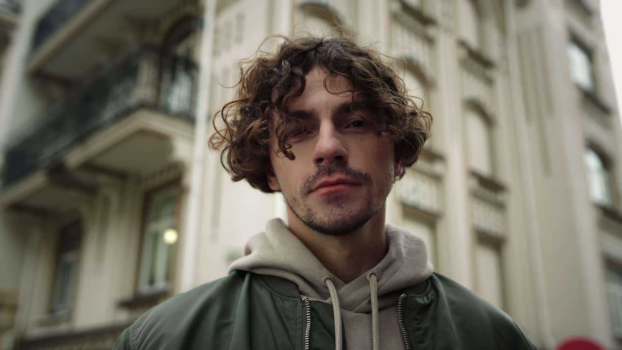 젊은 남자가 야외에서 카메라를 찾고 있습니다. 집중된 남자가 도시 거리에서 카메라를 포즈합니다.