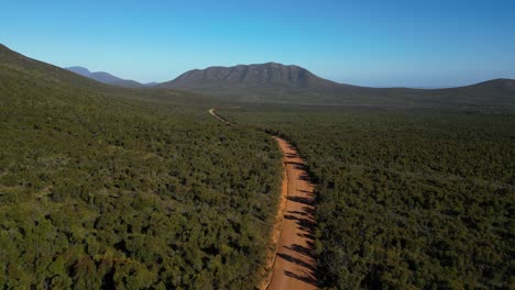 Toma-Aérea-De-Un-Camino-De-Tierra-Rojo-Vacío-Con-Montaña-A-Distancia-En-El-Interior-Australiano