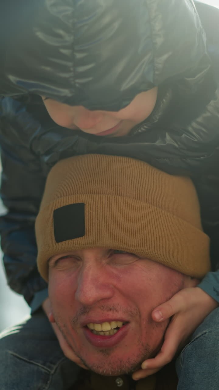 Close up of a father carrying his child on his shoulders, as the child play with his chin and he looks tired as his face becomes red because of the child we
