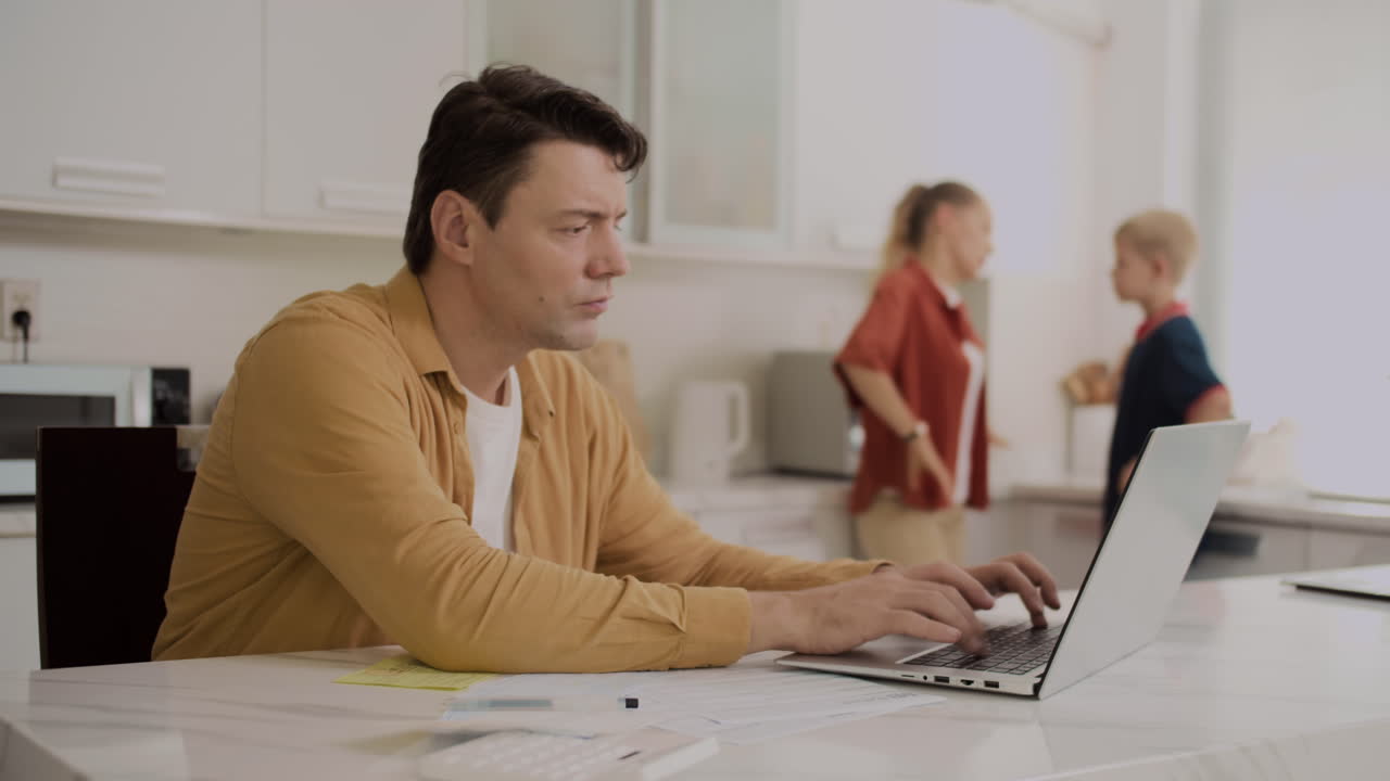 Homem pagando contas on-line enquanto sua esposa e filho discutem ao fundo