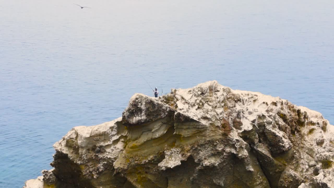 Aerial dolly along rugged rocky cliffs of Coronado Islands, Mexico, with crashing waves along the shore, tilt down to reveal fishermen on boat in ocean