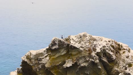 aerial dolly along rugged rocky cliffs of coronado islands, mexico, with crashing waves along the shore, tilt down to reveal fishermen on boat in ocean