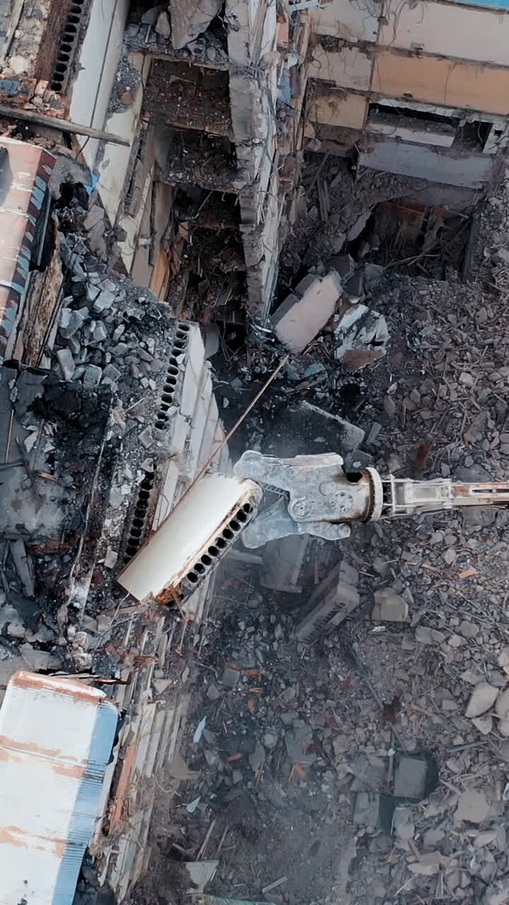 Bulldozer con brazo mecánico. Losa de hormigón cayendo. Excavadora demoliendo ruinas para un nuevo proyecto de construcción. Volando sobre una destrucción. Video vertical