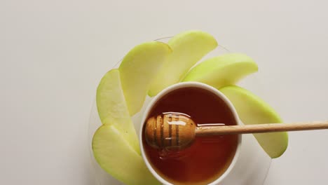 Video-of-honey-in-jar-and-apple-slices-lying-on-white-surface