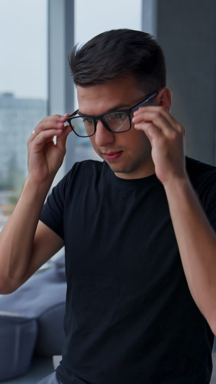 Man adjusting glasses and smiling in front of a window