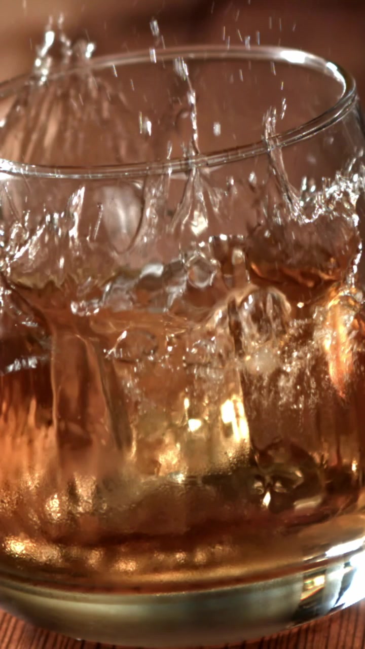 Cubo di ghiaccio che cade al rallentatore in un bicchiere di whisky con schizzi