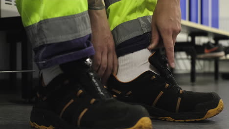 Male-wood-worker-readies-himself-for-shift-at-wood-mass-facility-by-lacing-up-work-boots-with-steel-toed-soles-getting-protective-equipment-in-order-safety-gear-forestry-industry-hazardous-environment