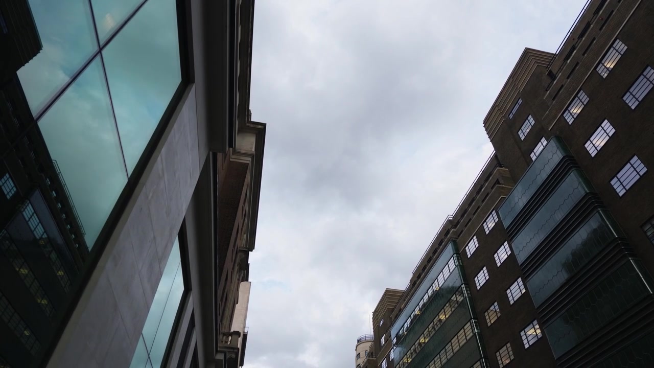 Una perspectiva ascendente enmarca edificios de ladrillo y cristal bajo un cielo gris cubierto de nubes