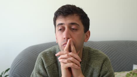 close-up of a stressed and worried man in his 30s, rubbing his face and staring into space