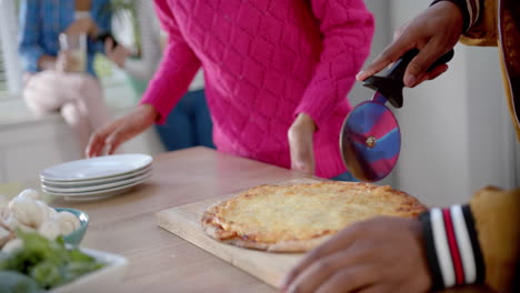 Happy-diverse-group-of-teenage-friends-cooking-and-cutting-pizza-in-kitchen,-slow-motion