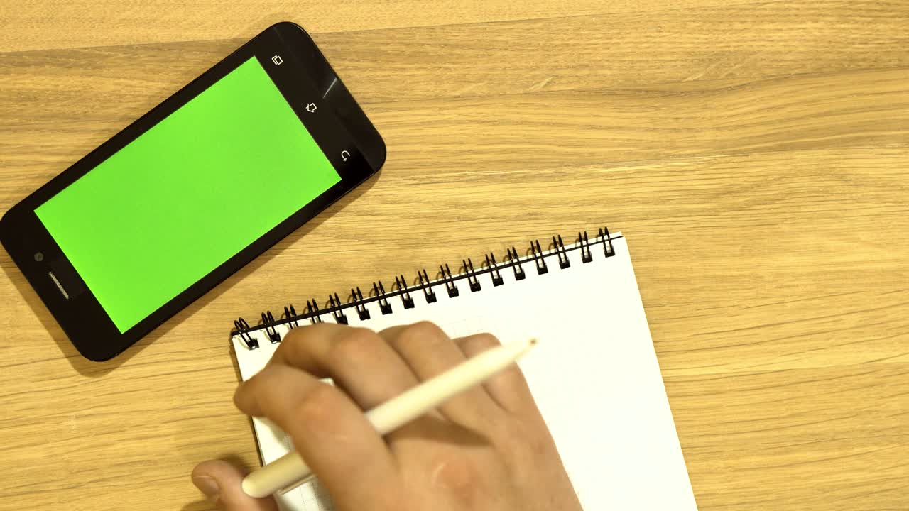 The specialist is sitting at the desk. Summarizing. Using smartphone. Green screen.