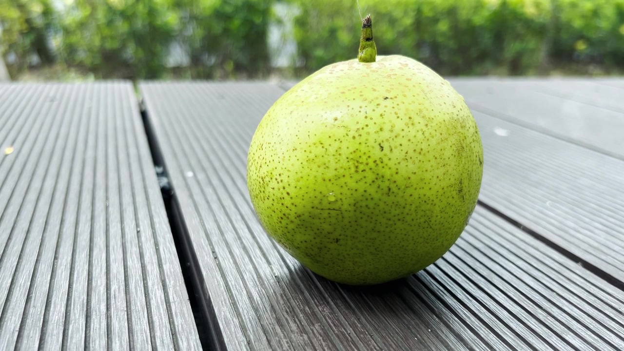 Una singola pera verde fresca appoggiata su una pedana di legno.