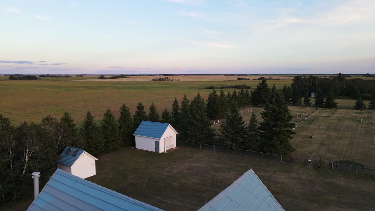 hermosa iglesia rural blanca y azul junto a un pequeño cementerio y dos cabañas al atardecer en alberta, canadá