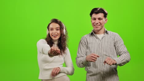a man and a woman are listening to music and dancing. they are smiling and have fun. the woman is wearing headphones. they are standing on a green background. green screen. 4k.
