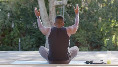Hombre-Afroamericano-Enfocado-Haciendo-Meditación-De-Yoga-En-Cubierta-En-Un-Jardín-Soleado,-Cámara-Lenta