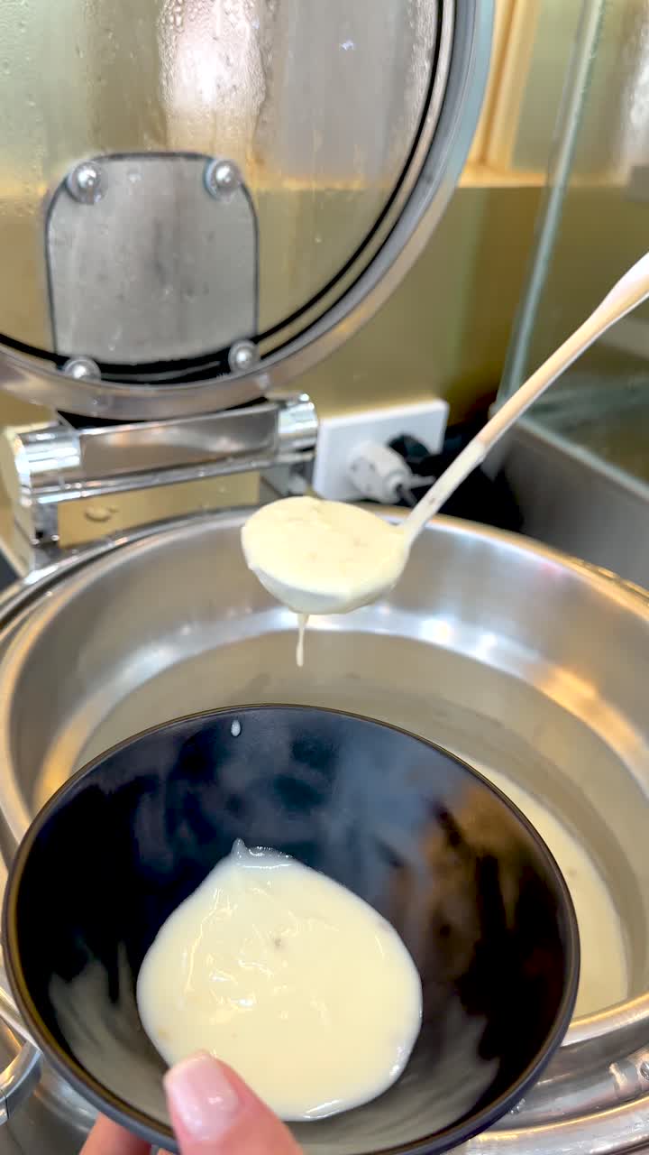 Close-up shot of a person ladling hot creamy soup from a metal warmer into bowls