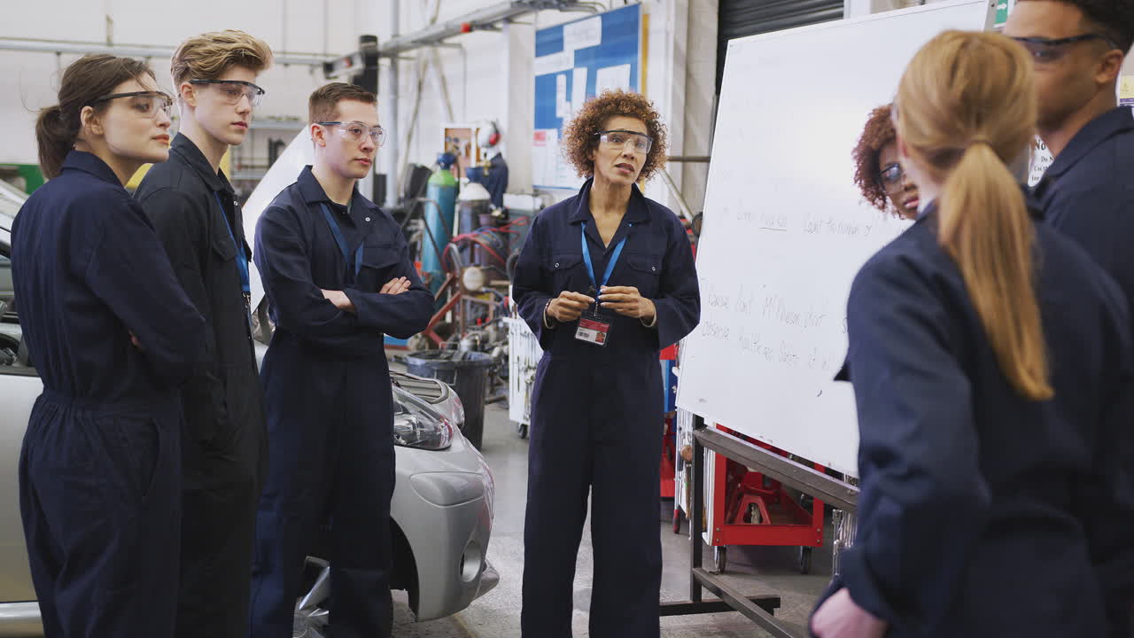 Students Studying Auto Mechanic Apprenticeship At College Asking Female Tutor Questions
