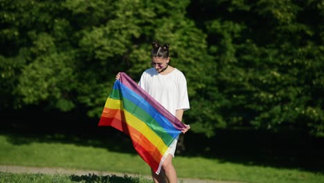 una mujer joven sosteniendo una bandera arco iris en un parque