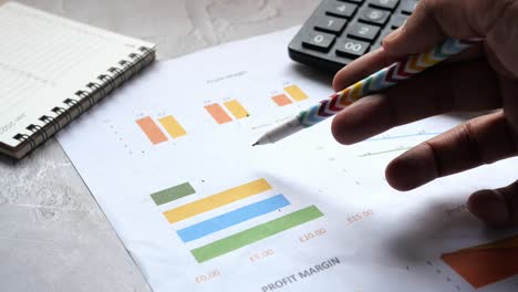 Man-hand-with-pen-analyzing-bar-chart-on-paper