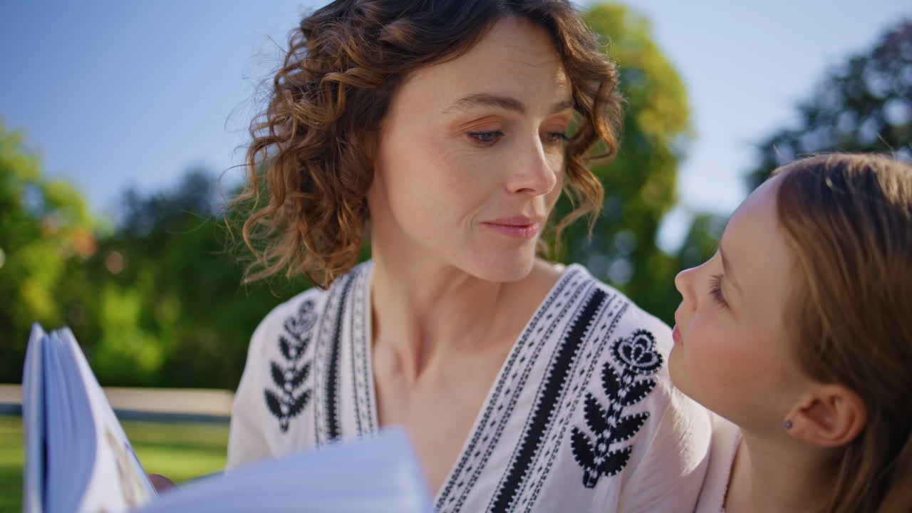 Mom kid enjoying novel together at summer park closeup. Woman daughter talking