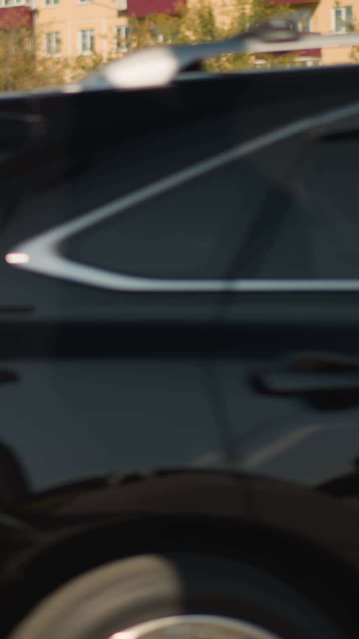 밝은 한낮의 햇살 아래 횡단보도를 가로지르는 빠른 자동차의 블러 효과, 멀리 보이는 주차된 차량 행렬과 아파트 단지, 모션 블러와 그림자가 드리워진 교통 표지판, 긴장감 넘치는 통근자들의 흐름과 다급한 거리의 모습