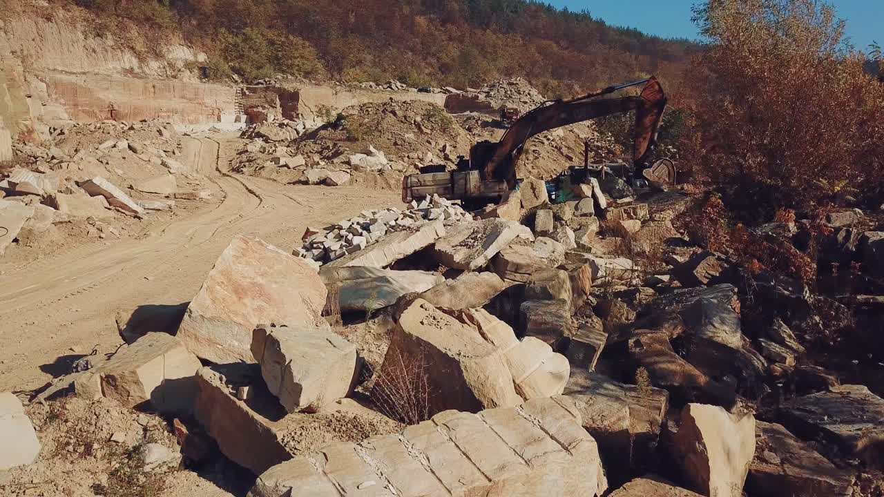 professional equipment are working in the quarry with stones on the background of a hill with a forest. View of the sand quarry. Camera motion straight