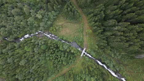 Drohne-Von-Oben-Nach-Unten-über-Einen-Bach-Mit-Einem-Pfad,-Der-Ihn-Mit-Einer-Brücke-In-Norwegen-überquert