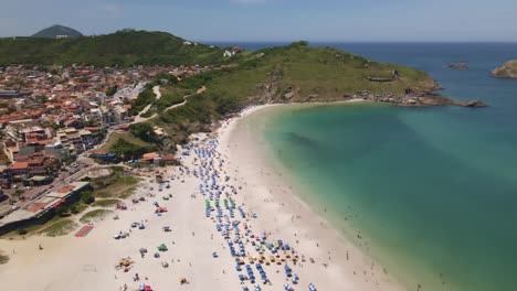 ciudad y la costa del mar con la colina y las rocas con varias personas disfrutando de un día soleado en la playa con las sombrillas un hermoso lugar arraial do cabo brasil