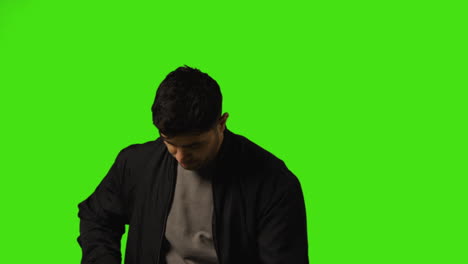 Young-Man-Answering-Call-On-Mobile-Phone-Standing-Against-Green-Screen-Studio-Background