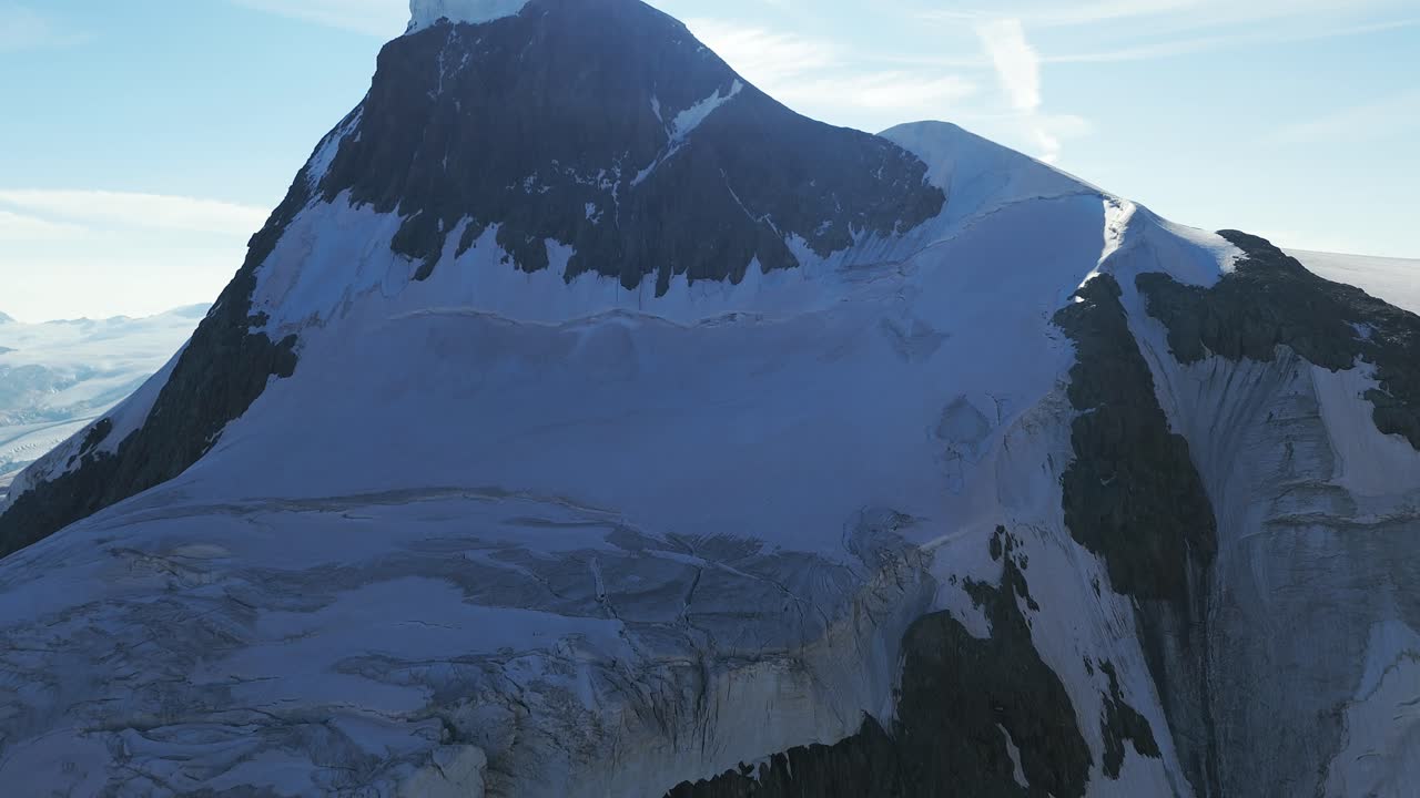 Aerial drone shot pushing in and tilting up to a close-up of the snow-covered peak of a mountain in the Swiss Alps