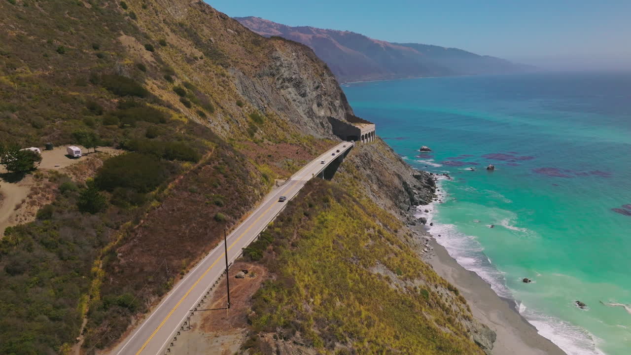 Two-lane highway with tunnels on the mountains of California coastline. Beautiful view of azure ocean at the shore. Top view.