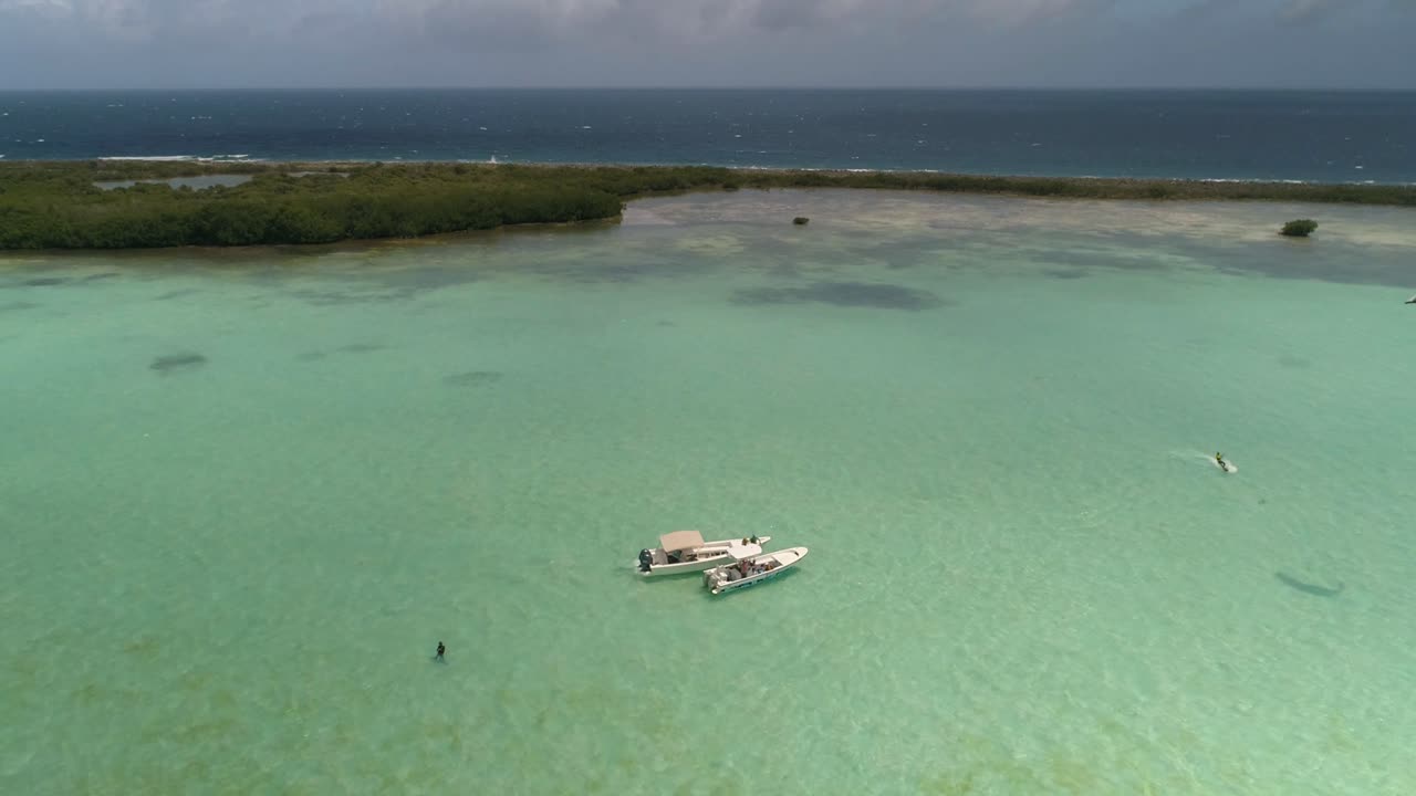 dos barcos amarrados esperando kitesurfistas volando alrededor de aguas turquesas, los roques