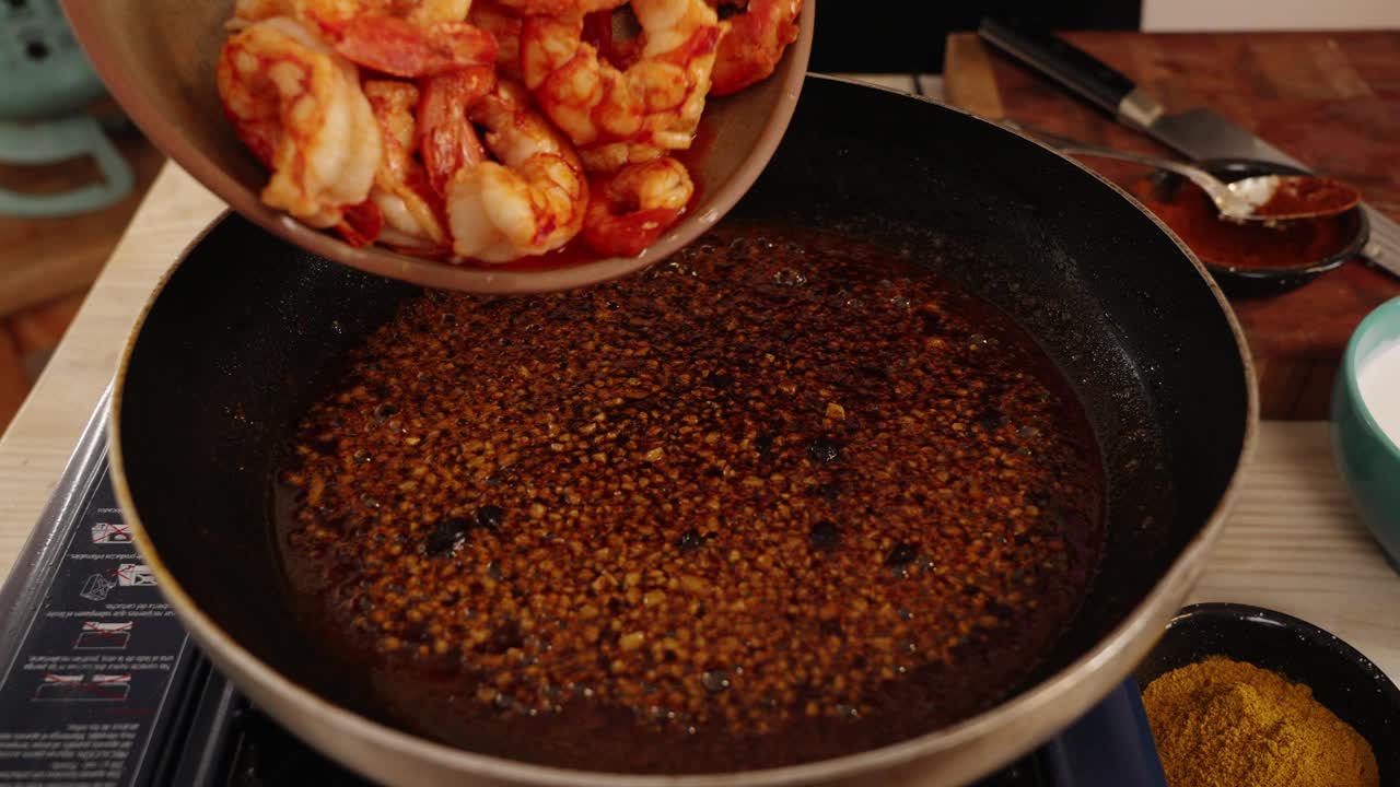 dejando caer lentamente deliciosos camarones cocidos en una burbujeante salsa picante de paprika con ajo, cubriendo el sabor de los camarones pelados, enriqueciendo el sabor y el aroma del plato de mariscos, toma de primer plano