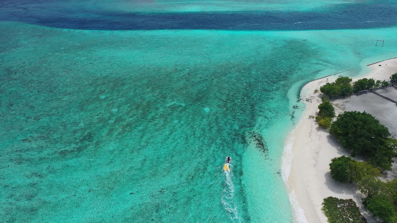 청록색 인도양 물에서 몰디브 섬의 하얀 모래 해변을 따라 항해하는 모터보트의 조감도