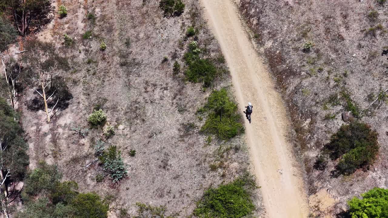 High angle drone shot follows a cyclist riding down a winding dirt mountain bike trail