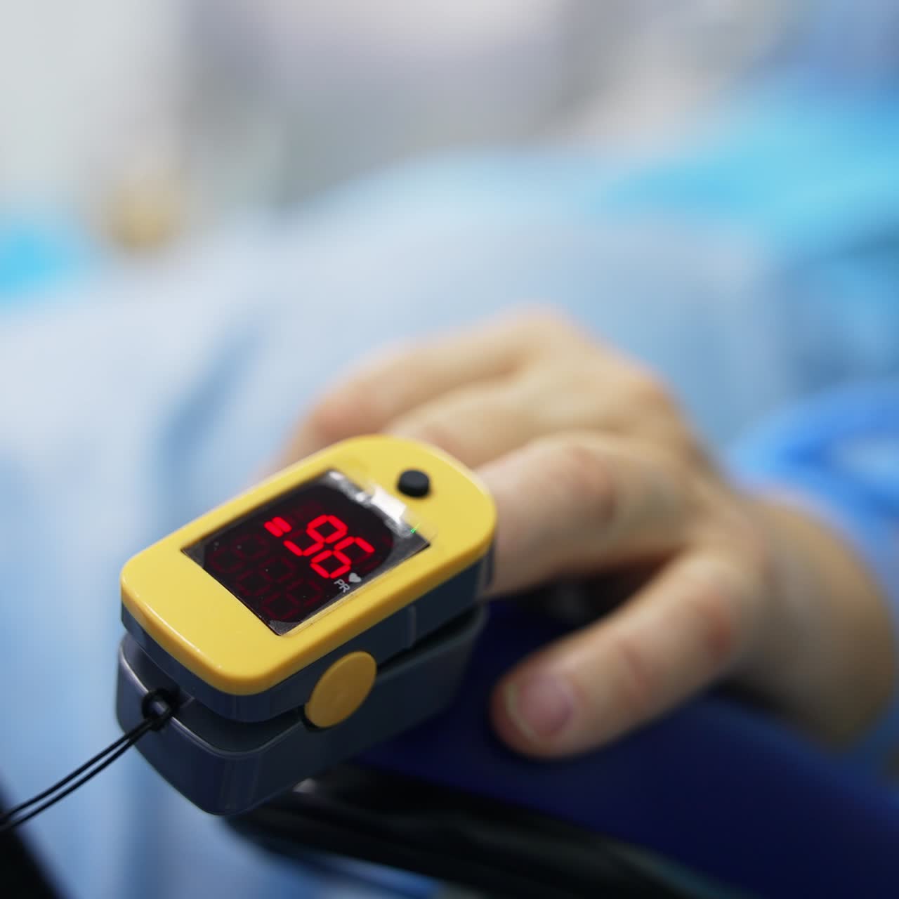 Hand of a patient with pulse oximeter on showing saturation. Close up. Ophthalmology operation in process. Blurred backdrop