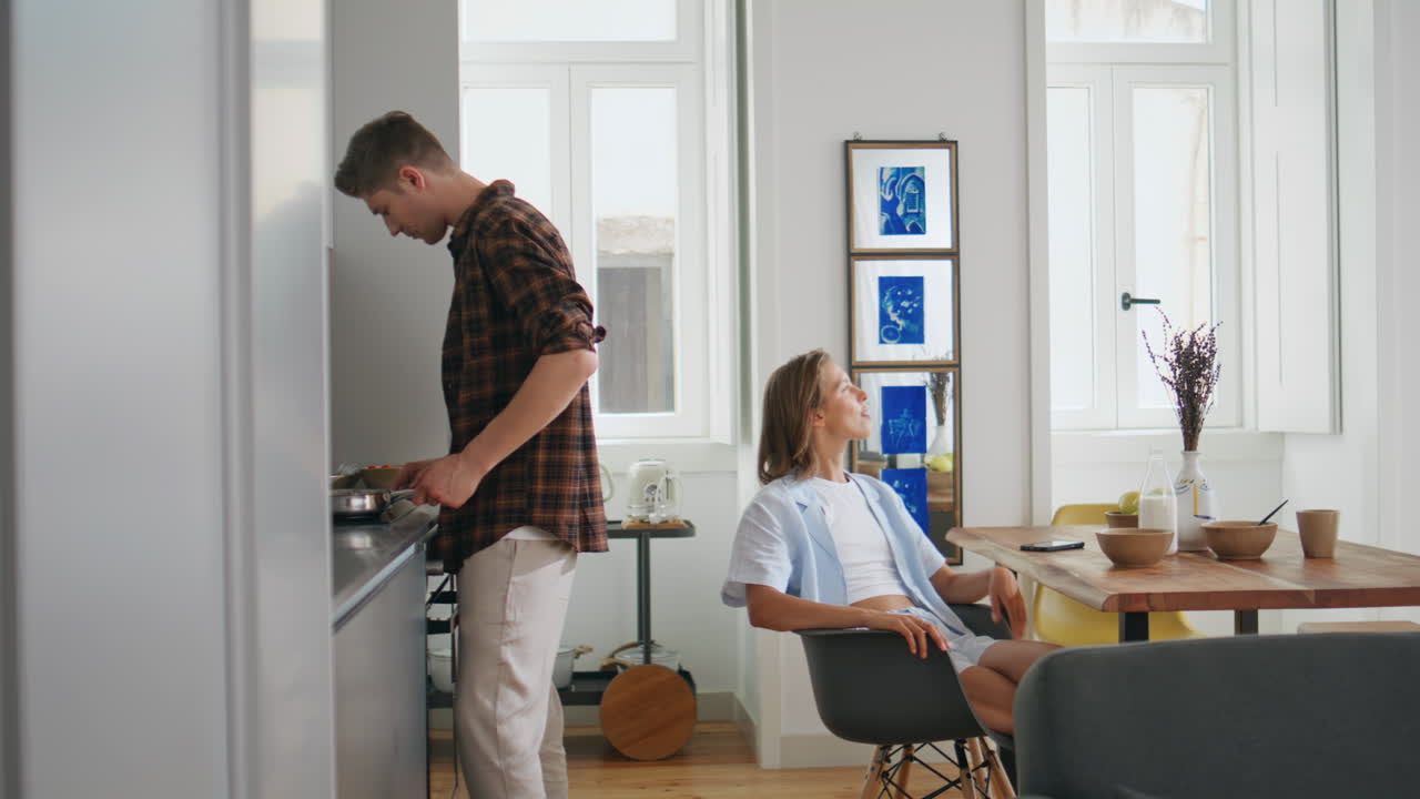 Man cooking breakfast home in morning. Relaxed wife watching husband resting