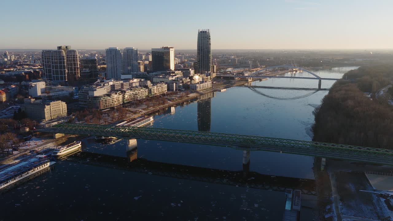 Vista aerea diurna dello skyline moderno di Bratislava lungo il fiume Danubio con ponti ed edifici di grande altezza. Luce invernale, riflessi calmi sull'acqua e paesaggio urbano contemporaneo (4K).