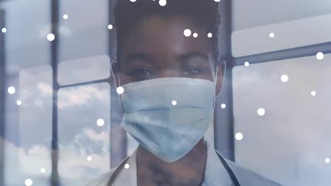White-spots-falling-against-portrait-of-african-american-female-doctor-wearing-face-mask