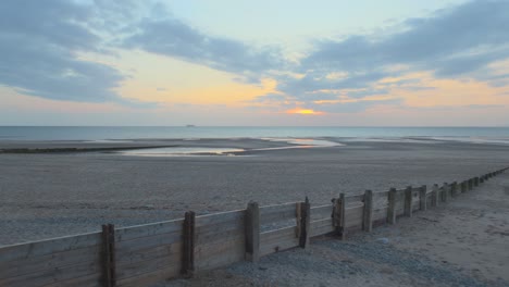 Rompeolas-De-Madera-Con-Barco-En-El-Horizonte-Aumento-Lento-Durante-La-Puesta-De-Sol-En-Cámara-Lenta-En-Fleetwood,-Lancashire,-Reino-Unido