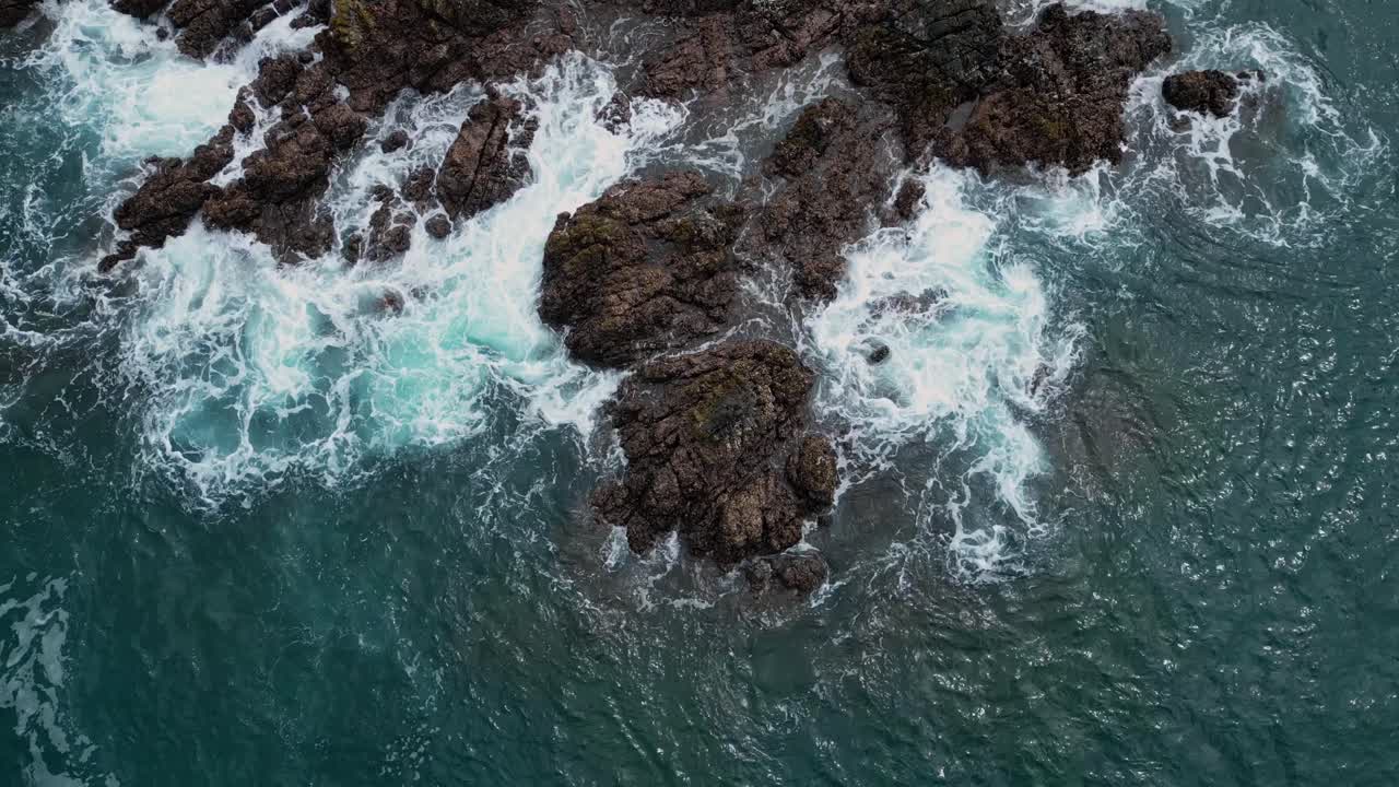 A captivating drone shot captures the dramatic beauty of rocky stones scattered along the shore, with the ocean waves crashing against them.