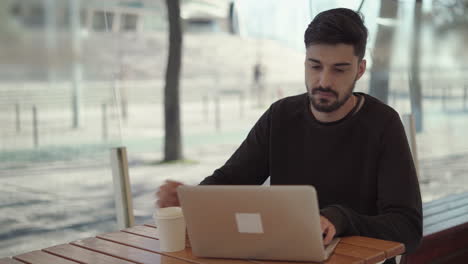 Hombre-Concentrado-Usando-Una-Computadora-Portátil-Y-Bebiendo-De-Un-Vaso-De-Papel