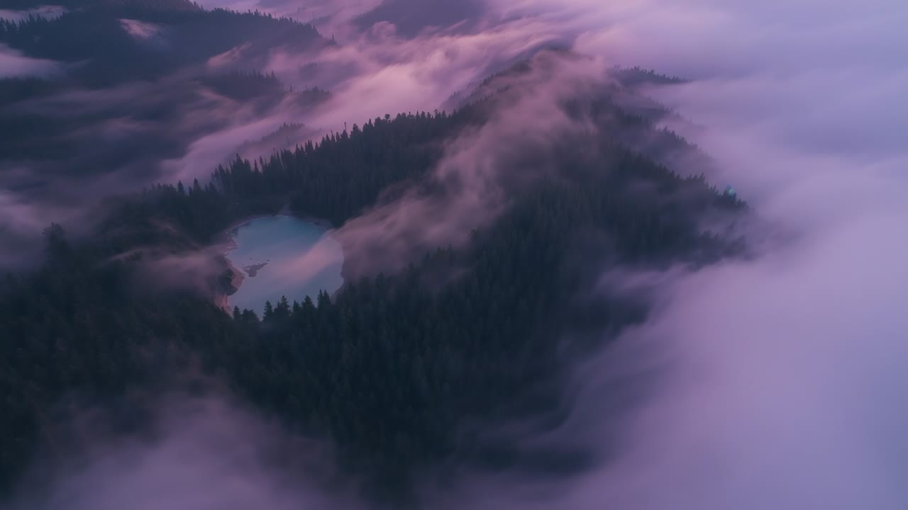 Wind shifting low clouds, aerial camera revealing forested ridge, shore and turquoise lake at dawn